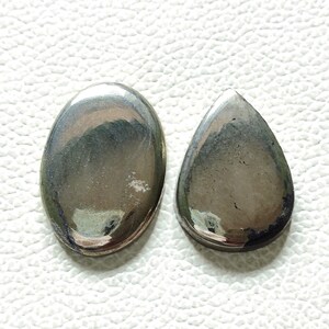 Può includere: Due cabochon di pietra preziosa di forma ovale, uno con forma a goccia. Le pietre sono di colore grigio scuro con un bagliore metallico.