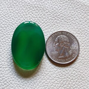 Può includere: Una pietra preziosa ovale di colore verde, delle dimensioni di una moneta da 25 centesimi di dollaro americano.
