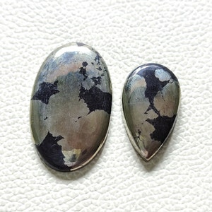 Può includere: Due cabochon di pietra preziosa, uno ovale e uno a forma di lacrima, con finitura metallica argentata e martellatura bianca e nera.