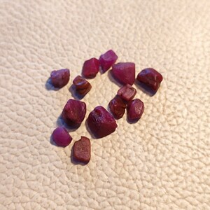 Może przedstawiać: Kolekcja małych, surowych, różowych rubinów. Kamienie szlachetne mają różne kształty i rozmiary.