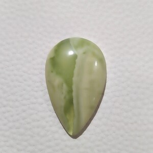 May include: A teardrop-shaped green and white gemstone cabochon. The stone has a smooth, polished surface and a translucent appearance.