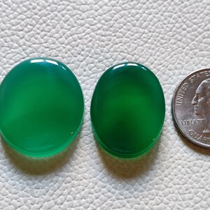 Può includere: Due cabochon di agata verde, uno rotondo e uno ovale, accanto a una moneta da un quarto di dollaro americano per il confronto delle dimensioni.
