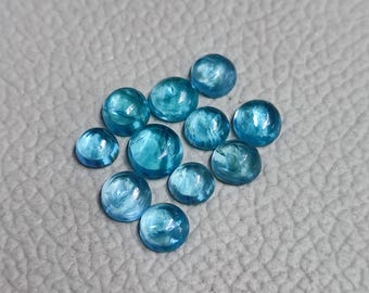 May include: A collection of eleven round, cabochon-cut gemstones. The gems are a vibrant, translucent teal color with internal veining, set against a gray textured surface. The gemstones vary slightly in size.