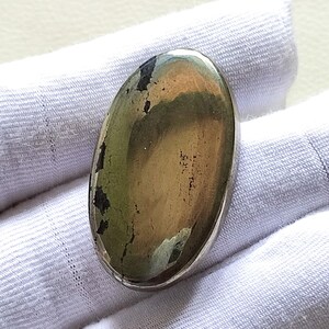 May include: Oval shaped cabochon gemstone with a metallic gold and green colour. The stone is set in a silver bezel.