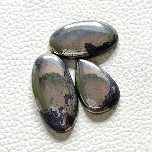 Può includere: Tre pietre preziose di pirite di forma ovale, di colore argento e nero metallizzato. Le pietre hanno una superficie liscia e lucida.
