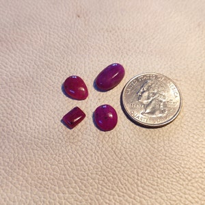 Może przedstawiać: Cztery różowe kamienie szlachetne o różnych rozmiarach i kształtach, obok amerykańskiej ćwierćdolara. Kamienie szlachetne są prawdopodobnie rubinami.