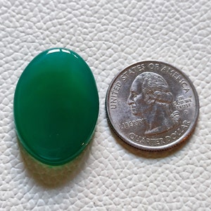 Può includere: Un cabochon di agata verde liscio di forma ovale, circa delle dimensioni di una moneta da 25 centesimi di dollaro americano.