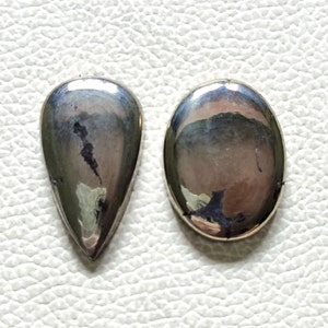 Può includere: Due cabochon di pietra preziosa, uno a forma di lacrima e uno ovale, entrambi con una finitura metallica argentata.