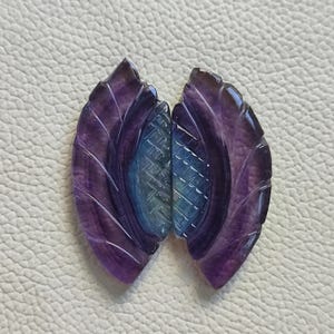 以下が含まれることがあります： 紫と青の蛍石の宝石でできた、彫刻された葉が2枚。葉は渦巻き模様に彫刻されており、滑らかで磨かれた仕上げになっています。