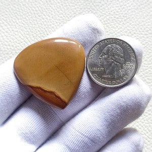 Può includere: Una pietra preziosa a forma di cuore, lucidata, di colore marrone e arancione su uno sfondo bianco. La pietra preziosa è circa delle dimensioni di una moneta da 25 centesimi di dollaro americano.