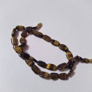 May include: A brown and gold tiger's eye gemstone necklace with oval-shaped beads.