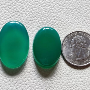 Può includere: Due pietre preziose ovali verdi lucide accanto a una moneta. Le pietre hanno una superficie liscia e lucida e variano leggermente di dimensioni. La moneta è d'argento e mostra il profilo di una persona. Le pietre misurano circa 2,5 cm.