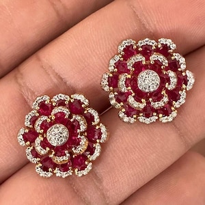 May include: A pair of gold earrings with a flower design. The earrings are made with red and white gemstones.
