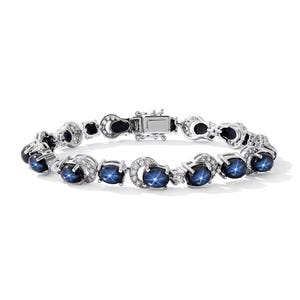 May include: A silver-toned link bracelet featuring a series of oval-shaped dark blue star sapphires, each displaying a distinct six-rayed star effect. The stones are set in metal frames accented with small, clear, round-cut stones and a box clasp.
