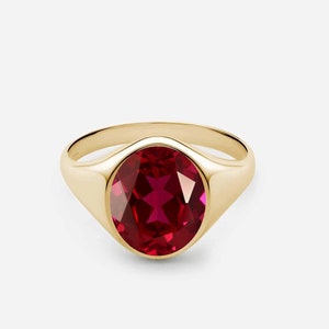 May include: A gold signet ring featuring a large, oval-shaped, red gemstone.