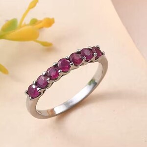 Könnte beinhalten: Ein silberner Bandring mit einer Reihe kleiner, runder, roter Edelsteine.