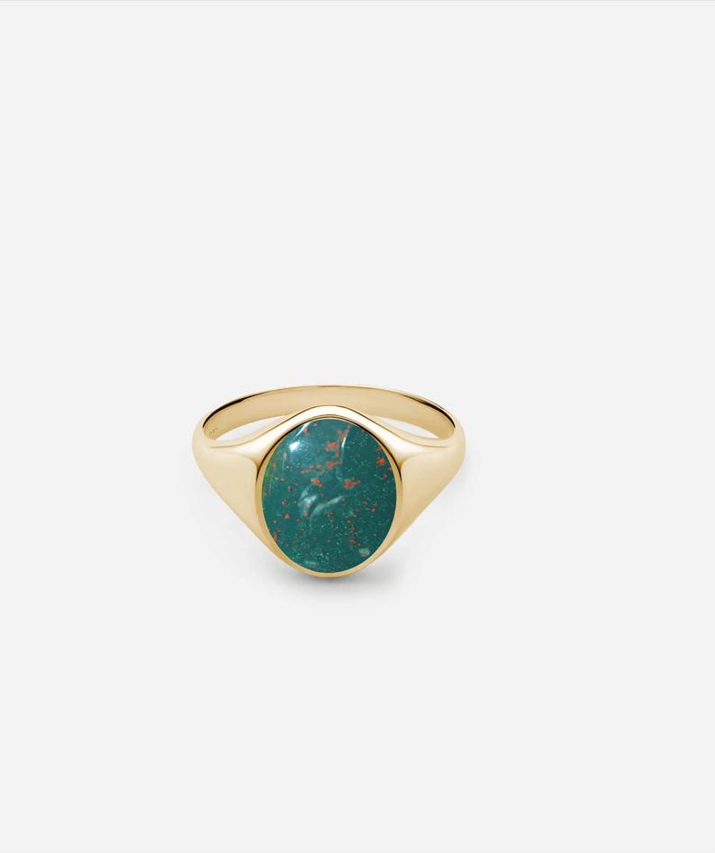 May include: A gold signet ring with a green oval gemstone. The gemstone has a marbled pattern with hints of brown.