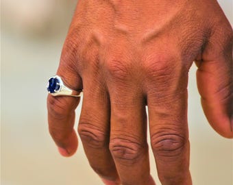 May include: A silver ring with a dark blue oval gemstone. The ring is on a person's finger.