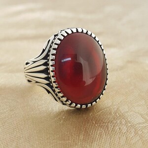Könnte beinhalten: Ein silberner Ring mit einem großen, ovalen, roten Edelstein, der in einer dekorativen silbernen Fassung sitzt.