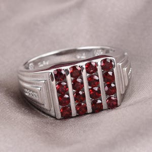 May include: A silver ring with a rectangular red gemstone setting. The ring has a textured band with a decorative design.