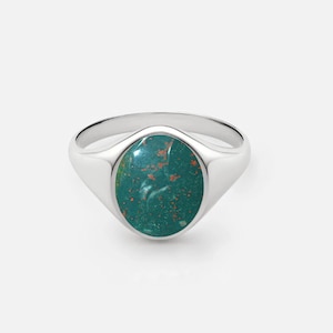 May include: A silver signet ring with a green oval gemstone. The gemstone has a mottled pattern of orange and green.
