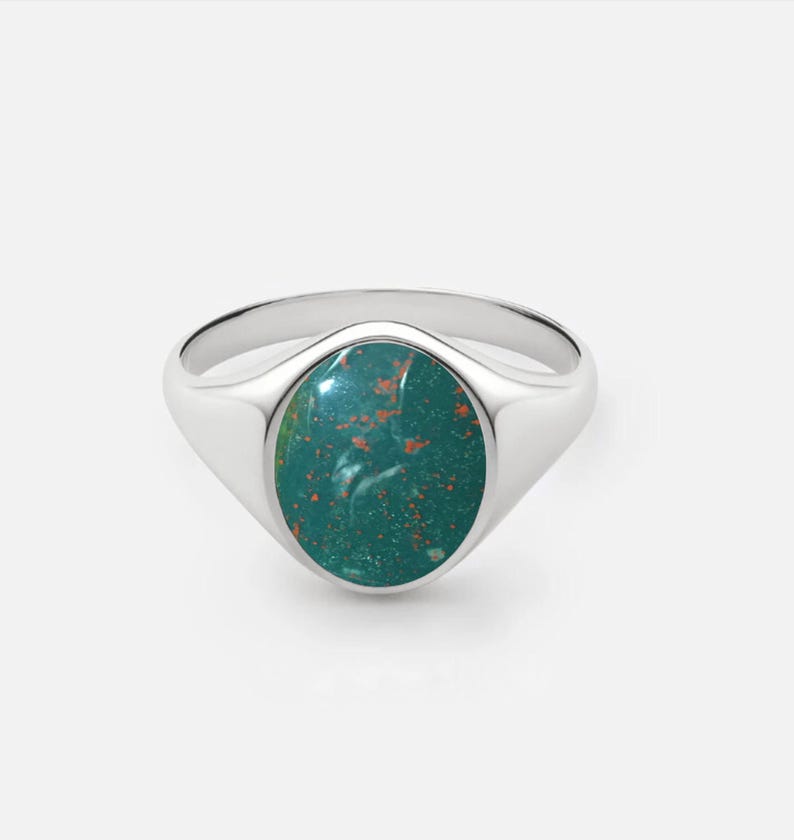 May include: A silver signet ring with a green oval gemstone. The gemstone has a mottled pattern of orange and green.