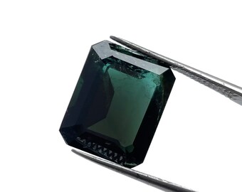 May include: A dark green emerald cut gemstone held by tweezers.