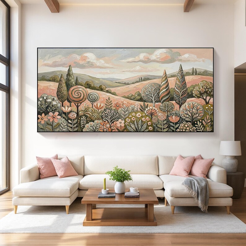 Pu&ograve; includere: Un grande dipinto di paesaggio incorniciato raffigura una scena di campagna stilizzata. L'opera presenta colline, alberi e fiori in tenui tonalit&agrave; di rosa, verde e beige. Il dipinto &egrave; appeso sopra un divano componibile color crema con cuscini rosa.