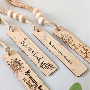May include: Four wooden bookmarks with different quotes and designs. The bookmarks are strung together with twine and wooden beads. The quotes include "Lost in a book", "Just one more chapter...", "A book keeps reality", and "So many books, so little time".
