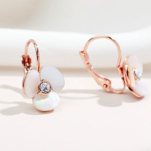 Peut inclure: Boucles d'oreilles créoles en or rose avec un motif de fleur blanche et un strass transparent au centre.