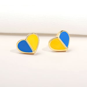 Può includere: Un paio di orecchini a forma di cuore dorati con smalto blu e giallo. Gli orecchini sono divisi a metà, con una metà blu e l'altra metà gialla.