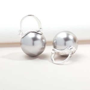 May include: A pair of silver earrings featuring large, round, grey pearls. The earrings have a simple, elegant design.
