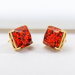 May include: A pair of gold stud earrings with square-shaped red glitter stones.