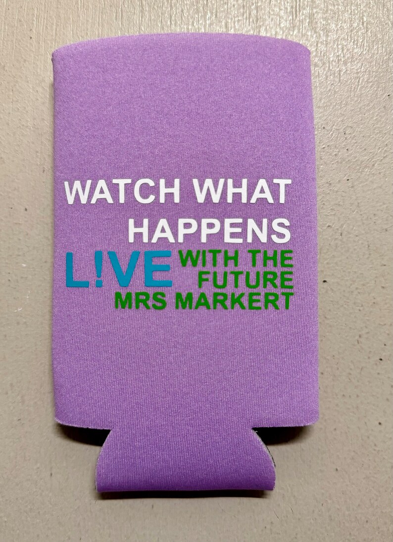 May include: A lavender-colored can cooler with the text "WATCH WHAT HAPPENS LIVE WITH THE FUTURE MRS MARKERT" in white, teal, and green. The cooler is designed to keep beverages cold and features a cut-out for easy gripping.