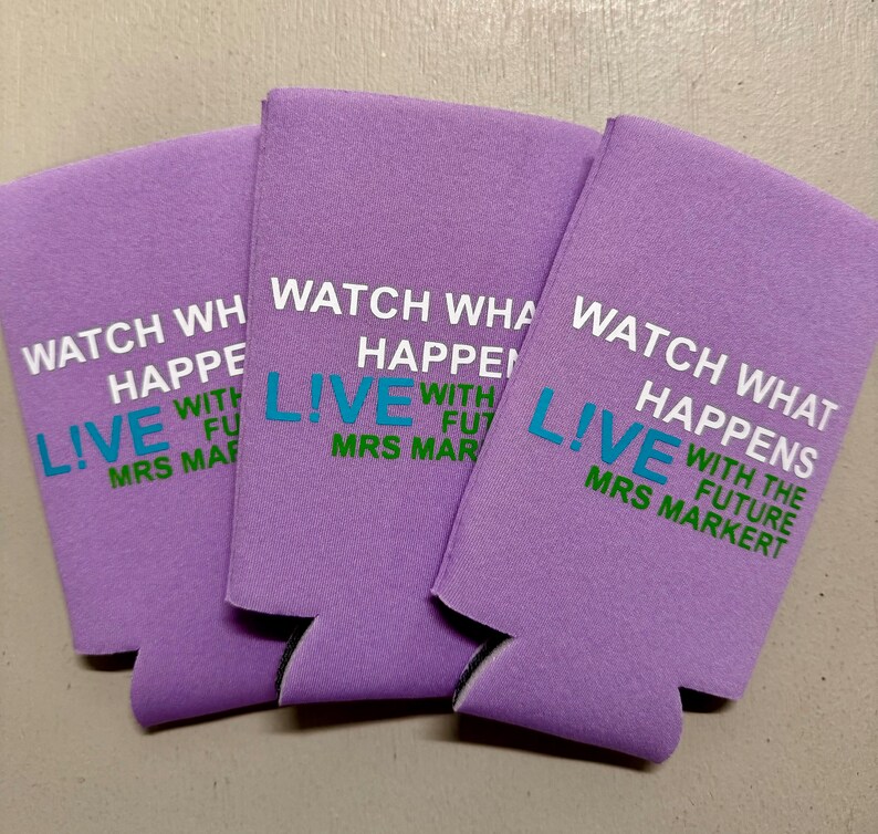 May include: Three lavender-colored can coolers with the text "WATCH WHAT HAPPENS LIVE WITH THE FUTURE MRS MARKERT" printed in white, teal, and green. The coolers are made of a foam-like material.