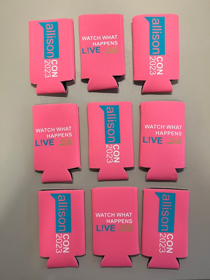 May include: Pink can coolers with teal and white text. The text includes "allison CON 2023" and "WATCH WHAT HAPPENS LIVE". The coolers are made of a foam material and are designed to keep beverages cold.