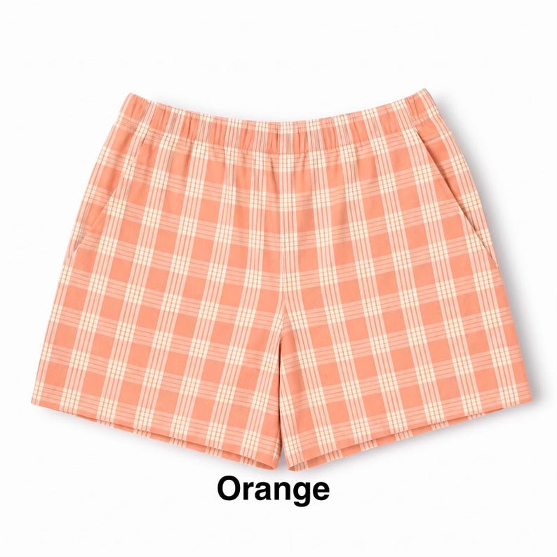 K&ouml;nnte beinhalten: Orangefarbene Shorts mit wei&szlig;em Karomuster, elastischem Bund und Seitentaschen. Der Stoff zeigt ein durchgehendes, gleichm&auml;&szlig;iges Gitterdesign. Das Wort Orange ist in schwarzer Schrift unter der Shorts auf wei&szlig;em Hintergrund gedruckt.
