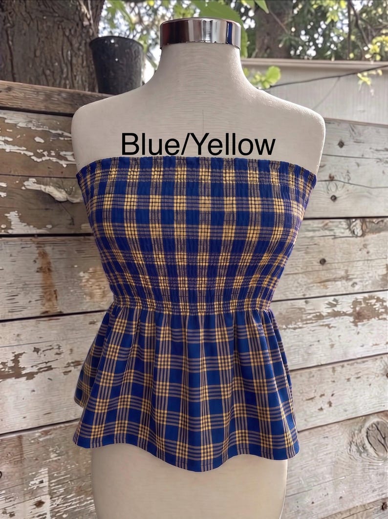 Peut inclure: Un haut bustier sans bretelles avec un motif &agrave; carreaux bleu et jaune, dot&eacute; d'un corsage smock&eacute; et d'un ourlet &agrave; basque &eacute;vas&eacute;. Le texte Blue/Yellow est imprim&eacute; sur la partie sup&eacute;rieure du v&ecirc;tement, pr&eacute;sent&eacute; sur un buste de mannequin.