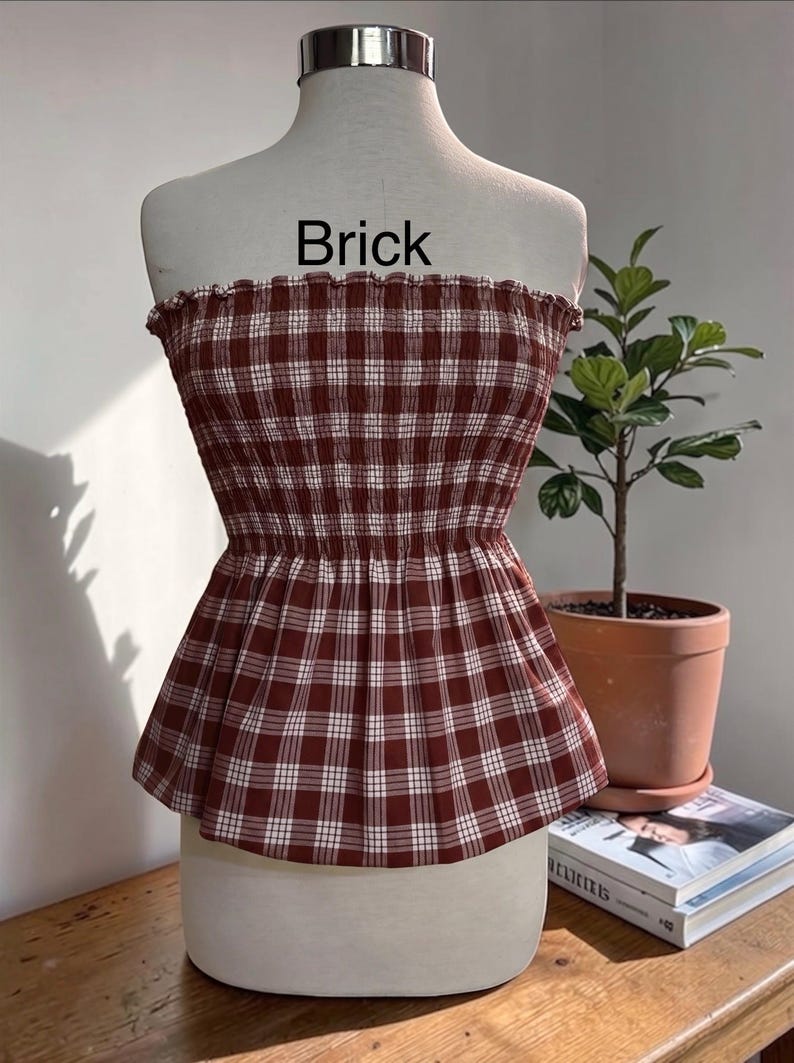 Peut inclure: Un haut bustier sans bretelles &agrave; motif &eacute;cossais rouge brique et blanc. Le v&ecirc;tement pr&eacute;sente un corsage smock&eacute; et &eacute;lastique avec un bord sup&eacute;rieur volant&eacute; et un ourlet &agrave; basque &eacute;vas&eacute;. Le mot Brick est imprim&eacute; en noir au-dessus du v&ecirc;tement.