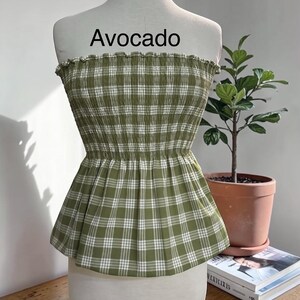 Peut inclure: Un haut bustier sans bretelles &agrave; motif &eacute;cossais vert olive et blanc. Le v&ecirc;tement pr&eacute;sente un corsage smock&eacute; et &eacute;lastique avec un bord sup&eacute;rieur volant&eacute; et un ourlet &agrave; basque &eacute;vas&eacute;. Le mot Avocado est imprim&eacute; en noir au-dessus du v&ecirc;tement.