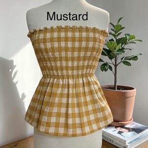 Peut inclure: Un haut bustier sans bretelles &agrave; motif &eacute;cossais jaune moutarde et blanc. Le v&ecirc;tement pr&eacute;sente un corsage smock&eacute; et &eacute;lastique avec un bord sup&eacute;rieur volant&eacute; et un ourlet &agrave; basque &eacute;vas&eacute;. Le mot "Mustard" est imprim&eacute; en noir au-dessus du haut.