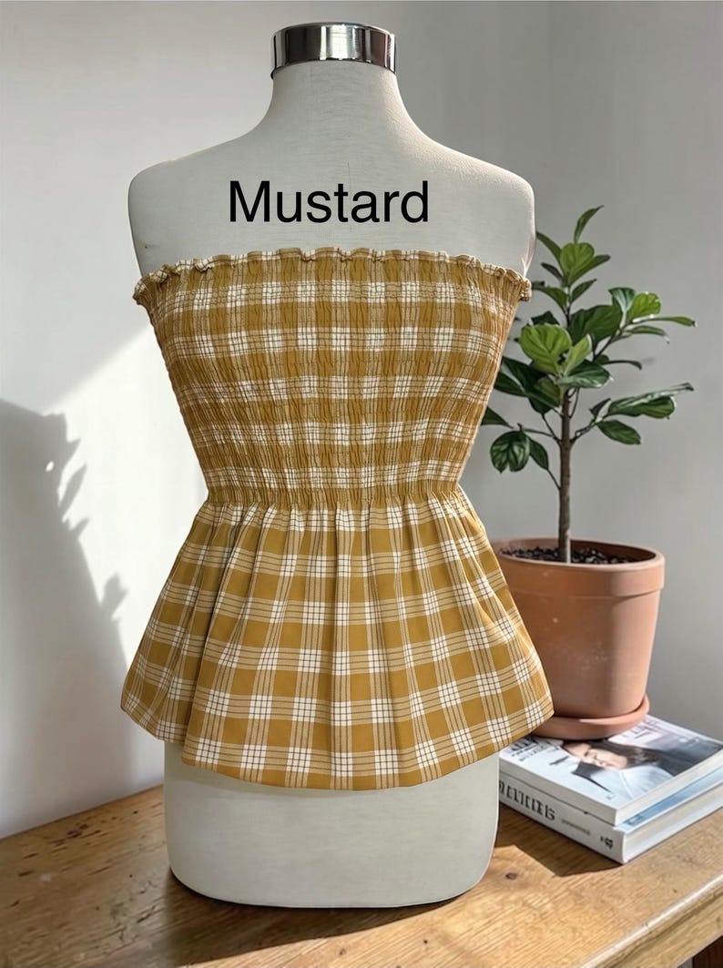Peut inclure: Un haut bustier sans bretelles &agrave; motif &eacute;cossais jaune moutarde et blanc. Le v&ecirc;tement pr&eacute;sente un corsage smock&eacute; et &eacute;lastique avec un bord sup&eacute;rieur volant&eacute; et un ourlet &agrave; basque &eacute;vas&eacute;. Le mot "Mustard" est imprim&eacute; en noir au-dessus du haut.