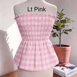 Peut inclure: Un haut sans bretelles rose clair avec un motif &agrave; carreaux blanc, dot&eacute; d'un corsage smock&eacute; &eacute;lastique et d'un ourlet &agrave; volants. Le texte 'Lt Pink' est imprim&eacute; au-dessus du v&ecirc;tement, pr&eacute;sent&eacute; sur un torse de mannequin.