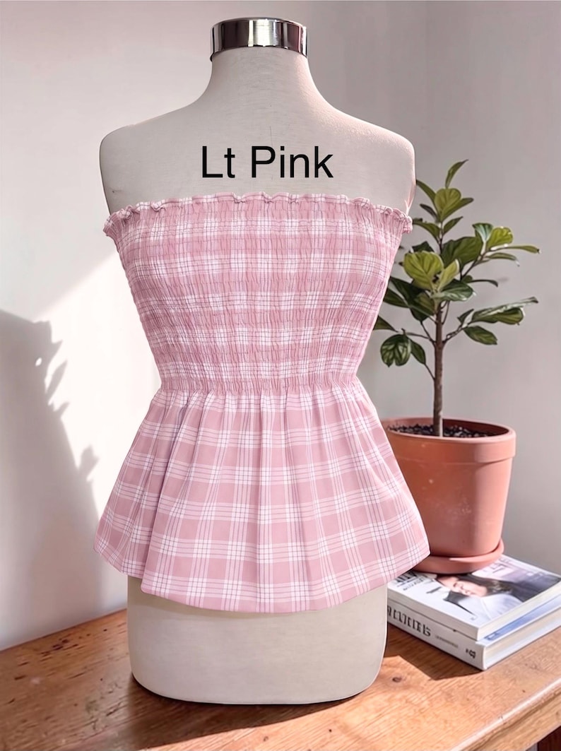 Peut inclure: Un haut sans bretelles rose clair avec un motif &agrave; carreaux blanc, dot&eacute; d'un corsage smock&eacute; &eacute;lastique et d'un ourlet &agrave; volants. Le texte 'Lt Pink' est imprim&eacute; au-dessus du v&ecirc;tement, pr&eacute;sent&eacute; sur un torse de mannequin.