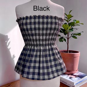 May include: A strapless tube top featuring a black and white plaid pattern with a smocked, elasticized bodice and a flared peplum hem. The word Black is printed in the center above the garment on the display mannequin.