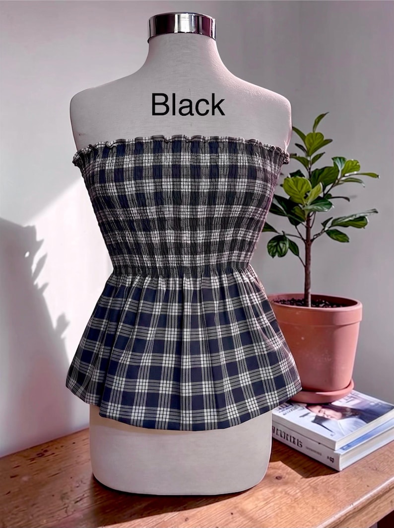 May include: A strapless tube top featuring a black and white plaid pattern with a smocked, elasticized bodice and a flared peplum hem. The word Black is printed in the center above the garment on the display mannequin.