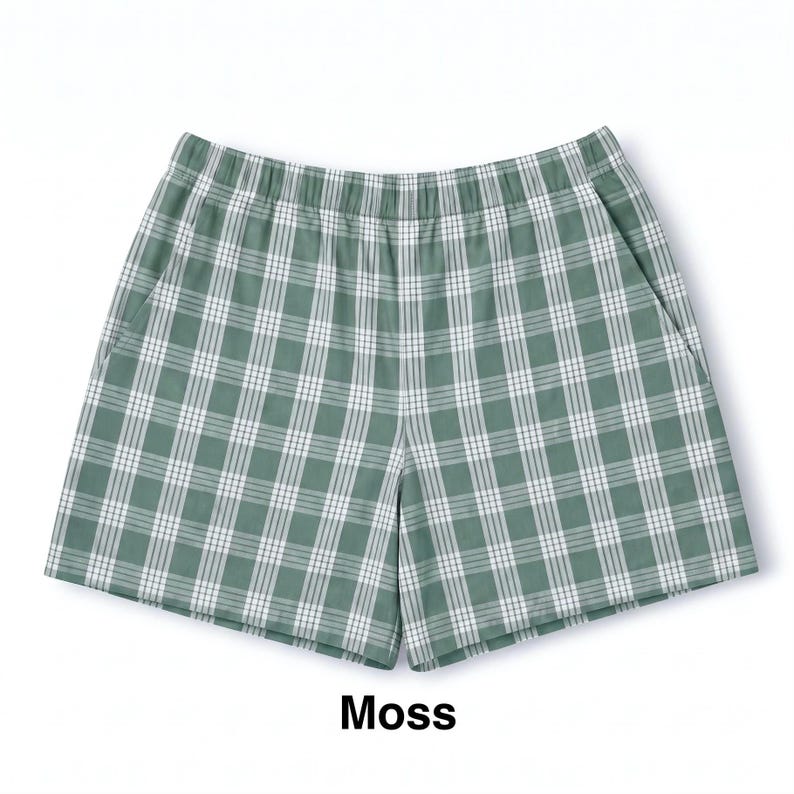 K&ouml;nnte beinhalten: Moosgr&uuml;ne Shorts mit wei&szlig;em Karomuster, elastischem Bund und Seitentaschen. Der Stoff zeigt ein durchgehendes, gleichm&auml;&szlig;iges Gitterdesign, wobei das Wort Moss in schwarzer Schrift unterhalb der Shorts abgedruckt ist.