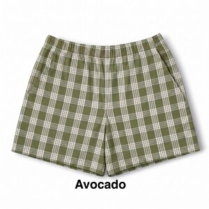 K&ouml;nnte beinhalten: Olivgr&uuml;ne Shorts mit einem wei&szlig;en und dunkelgr&uuml;nen Karomuster, ausgestattet mit einem elastischen Bund und zwei Seitentaschen. Das Wort Avocado ist in schwarzer Schrift unter dem Kleidungsst&uuml;ck gedruckt, das einen geraden Saum hat.