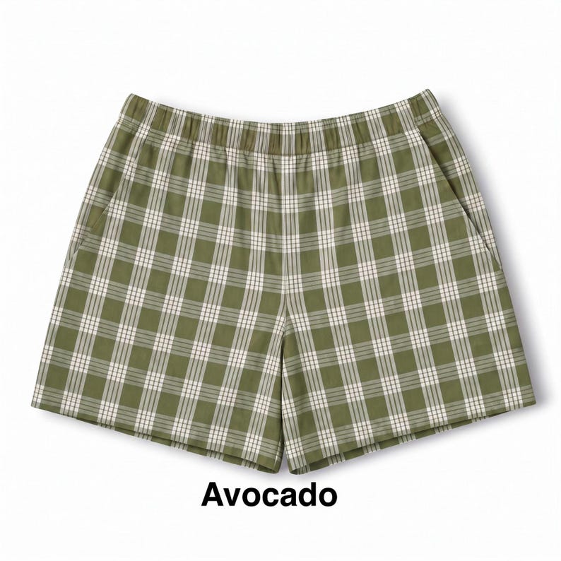 K&ouml;nnte beinhalten: Olivgr&uuml;ne Shorts mit einem wei&szlig;en und dunkelgr&uuml;nen Karomuster, ausgestattet mit einem elastischen Bund und zwei Seitentaschen. Das Wort Avocado ist in schwarzer Schrift unter dem Kleidungsst&uuml;ck gedruckt, das einen geraden Saum hat.