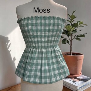 Peut inclure: Un haut bustier sans bretelles &agrave; motif &eacute;cossais vert mousse et blanc. Le v&ecirc;tement pr&eacute;sente un corsage smock&eacute; et &eacute;lastique avec un bord sup&eacute;rieur volant&eacute; et un ourlet &agrave; basque &eacute;vas&eacute;. Le mot Moss est imprim&eacute; en noir au-dessus du v&ecirc;tement.